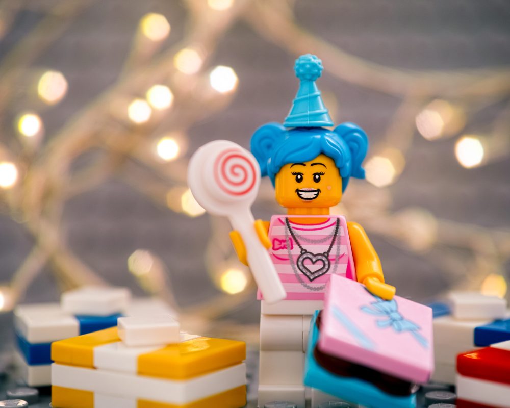 Tambov, Russian Federation - January 17, 2021 Lego birthday girl minifigure with lollipop and gifts against gray baseplate with christmas light background